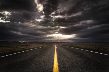 Ufukta dramatik bir günbatımına doğru uzanan sarı çizgili ıssız asfalt bir yol..