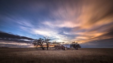 Old abandoned farmhouse at sunset on the eastern plans of Colorado in a rural countryside scene. The sky is full of brilliant colorful clouds. The rural landscape is barren and dry. clipart
