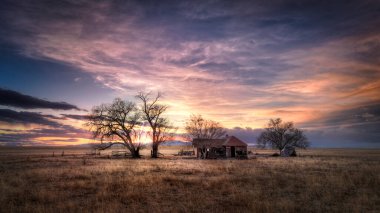 Old abandoned farmhouse at sunset on the eastern plans of Colorado in a rural countryside scene. The sky is full of brilliant colorful clouds. The rural landscape is barren and dry. clipart