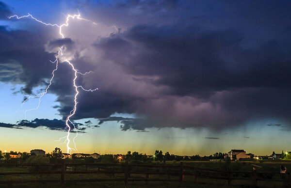 A bolt from the blue lighting strike from a thunder storm hits the ground in a rural neighborhood at sunset. 