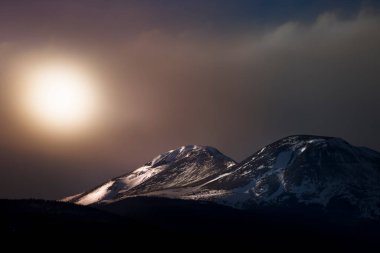 Colorado 'da turuncu bir gün batımının altında iki kar tanesi Rocky Dağı zirvesini kapladı. Sahne çok karamsar ve rüya gibi görünüyor..  