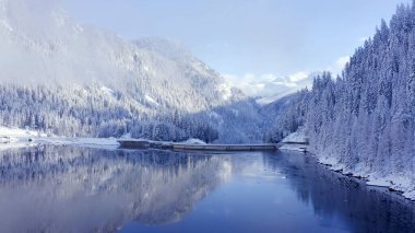 Dağların arasında, karlı bir ormandaki gölün üzerinde uçuyoruz.
