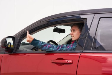 Woman driver shows middle finger, fuck you with a sign, with anger face. Concept of road rage.