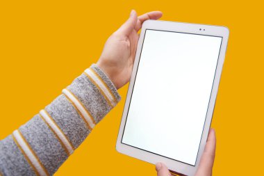 Close-up of female hands holding a tablet with an empty screen for text or image, on a GOLDEN yellow background. Concept of technology.