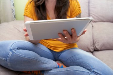 Cropped young woman in casual clothes uses a digital tablet while working from home. Concept of teleworking, gadgets, comfort, lifestyle.