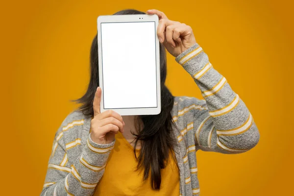 Female covering her face with a tablet pc over golden yellow background. Concept of technology, gadgets.