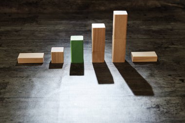 Tahta oyuncak blokları grafik şeklinde dizildi ve yeşil blok yükseldi. Sert gölgeli sade bir fotoğraf. Büyüme kavramı, borsa yükselişi ve umut.