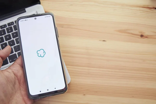 Madrid İspanya, 13 Haziran 2021; Ellerinde şirketin Wallapop uygulamasının logosu ve arka planında bilgisayar olan akıllı bir mobil cihaz var..