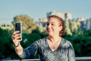Şehirde akıllı telefonuyla fotoğraf çeken olgun bir kadın. Kısa saçlı ve günlük kıyafetleri olan kızıl saçlı kadın. Yaşam tarzı kavramı