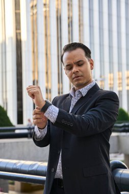 Resmi takım elbiseli şık Latin işadamı, modern ofis arkaplanına odaklanarak ve kendine güvenerek kollarını düzeltiyor.