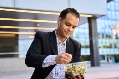 Takım elbiseli kendine güvenen Latin iş adamı taze salatanın tadını çıkarıyor, sağlıklı yaşam tarzını ve modern kurumsal dengeyi simgeliyor.