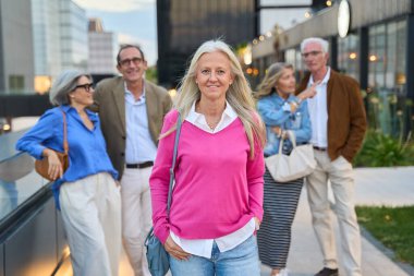 Bir grup gülümseyen olgun arkadaş kentte yürüyüş yapıyor, aktif bir üst düzey yaşam tarzı ve arkadaşlığı temsil ediyorlar.