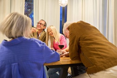 Bir grup kıdemli arkadaş neşeli bir akşam yemeği yiyor, konuşuyor ve gülüyor emekliliğin ve sosyal toplantının tadını çıkarıyorlar.