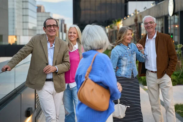 Bir grup kıdemli arkadaş dışarıda kaliteli zaman geçirir, modern bir şehir ortamında konuşur ve gülerler.