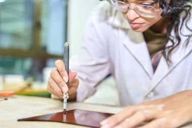 Kadın zanaatkar keskin bir aletle deri malzeme kesiyor, el yapımı özel bir ürünü bir atölyede yaratıyor.