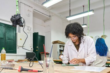 Cam parçalarıyla çalışan, laboratuvar önlüklü bir kadın stüdyo ortamında sanatsal bir tasarım hazırlıyor.