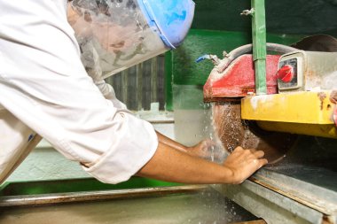 Islak testere kullanan koruyucu bir yüz kalkanı takan işçiler inşaat için bir fabrikada taş işliyorlar.