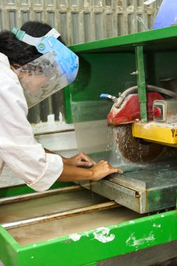 Islak testereyle atölyede cam ya da taş kiremit kesen bir işçi güvenlik için koruyucu yüz kalkanı takıyor.