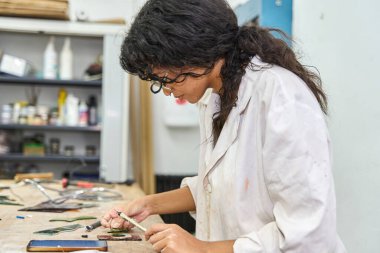 Laboratuvar önlüklü bir kadın çalışma tezgahında minicik vitray parçaları birleştiriyor.