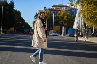 Kadın gülümsüyor ve bir şehir caddesinde yürüyor, güneşli bir sonbahar gününün tadını çıkarıyor. Kentsel yaşam tarzı ve günlük moda konsepti