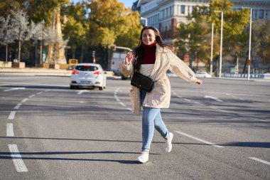 Güneşli bir günde şehir caddesinde koşan gülümseyen bir kadın. Sonbahar şehrinde neşeli bir an, enerjiyle hareket ediyor