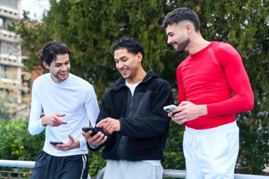 Akıllı telefonlara bakıp gülümseyen üç genç adam. İçerik paylaşımı ve şehirde bağlı kalmak