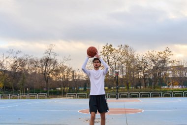 Sokak sahasında basketbol antrenmanı yapan erkek sporcu fitness ve antrenmanlara odaklanıyor.