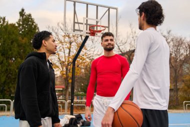 Bir grup farklı erkek, mavi şehir basketbol sahasında dostça sohbet ederken bir spor ve dostluk anı paylaşıyorlar.