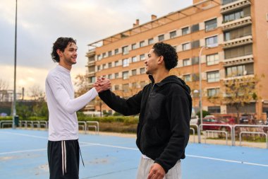 Bir basketbol sahasında takım çalışmasını ve sportmenliği göstererek, el sıkışarak selamlaşan arkadaşlar.