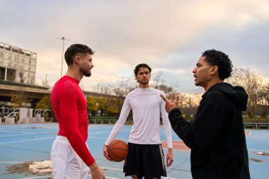 Üç arkadaş şehir dışındaki bir basketbol sahasında gündüz vakti oyun planları hakkında animasyon konuşuyorlar.