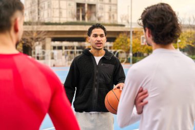 Atletik giyimli üç genç erkek arkadaş şehir dışındaki bir sahada basketbol oynarken strateji tartışıyorlar.