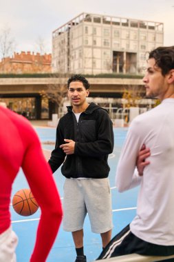 Bir basketbol maçı sırasında şehir ortamında açık bir sahada strateji tartışması yapan bir grup erkek.