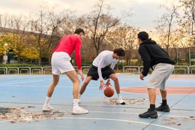 Genç erkekler mavi bir sahada basketbol topu sürüyor, sokak oyunu sırasında spor ve takım çalışması yapıyorlar.