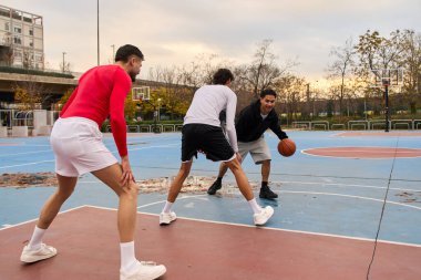 Açık havada basketbol oynamaktan hoşlanan üç genç adam şehir ortamında takım çalışması ve sağlıklı yaşam tarzları sergiliyor.