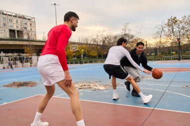 Dışarıda basketbol oynayan genç erkekler aktif olarak hareket ediyor ve top sürüyor. Rekabet, takım çalışması ve sağlıklı yaşam tarzı.