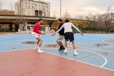 Açık havada basketbol oynayan üç genç adam, şehir kortunda takım çalışması ve spor yaşam tarzı sergiliyorlar.