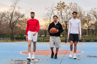 Gençler yağmurdan sonra açık bir basketbol sahasında birlikte yürüyor, aktif yaşam tarzı ve sporu kucaklıyorlar.