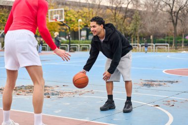 Dışarıda basketbol oynayan genç bir adam, şehir ortamında oynayan arkadaşlar aktif yaşam tarzını ve gençliği yansıtıyor.
