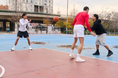 Basketboldan zevk alan üç adam, aktif olarak top sürüyor ve açık hava sahasından geçiyor, atletik bir yaşam tarzını destekliyor.