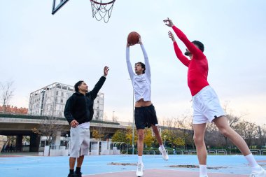 Üç genç adam yoğun bir sokak oyunu oynuyor, bir oyuncu şut için zıplıyor, iki defans oyuncusu blokluyor