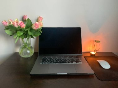 Beyaz arka planda güller ve mum ve ahşap masa olan dizüstü bilgisayar