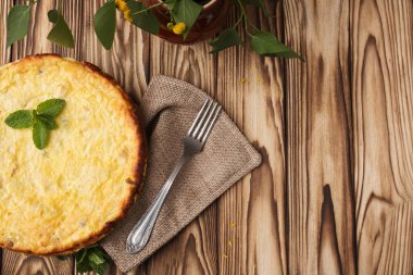 Ahşap zemin üzerinde yeşil nane yaprağı olan cheesecake. Tekstil peçetesinde demir çatal.