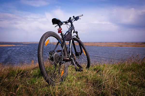 Black bike on the background of the river. Cloudy sky and green grass.