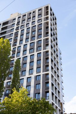 Mavi gökyüzüne karşı çok katlı bir bina. Aynalı pencereli, alt manzaralı yeni bir bina. Arkaplan yapısı: yüksek katlı, gökdelen, kule.