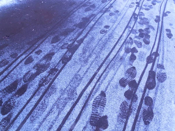 Footprints (shoe soles) and bicycle tire tracks on a thin layer of snow that recently fell on the asphalt.