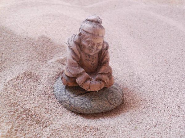 Souvenir netsuke (consumer goods) made of gypsum or cement. A figure on a rounded stone against a background of sand. Aura Zen, harmony, and meditation.