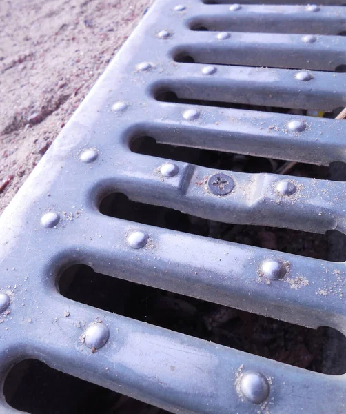 A drainage system that drains water from a gravel path in the park. A tray covered with a metal grate.