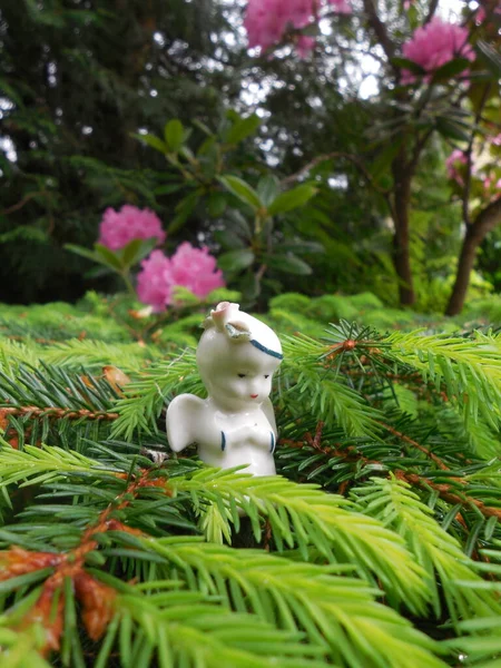 A small white angel (the subject is the property of the author of the photo) on the background of a blooming evergreen rhododendron Haaga.