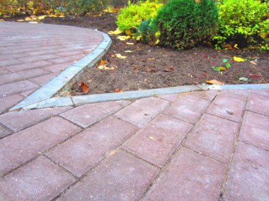 Bölgenin peyzajı. Karmaşık şeklin bir açıyla asfaltlanması dikdörtgen kırmızımsı fayanslardan yapılmıştır ve gri kaldırım taşıyla sınırlıdır. Çalıların yanında ve yere düşmüş yapraklarla.