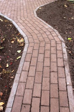 Yakın zamanda kırmızımsı dikdörtgen asfalt levhalarla döşenmiş, köşeli bir yol (virajlı) ve kaldırımlı bir platform. Her iki tarafta da düşen sonbahar yapraklarıyla kara toprak var..